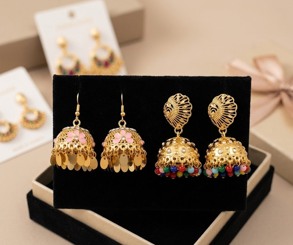 Gold-toned jhumka earrings displayed on a black velvet jewelry box, with matching earrings on white retail cards in the background.