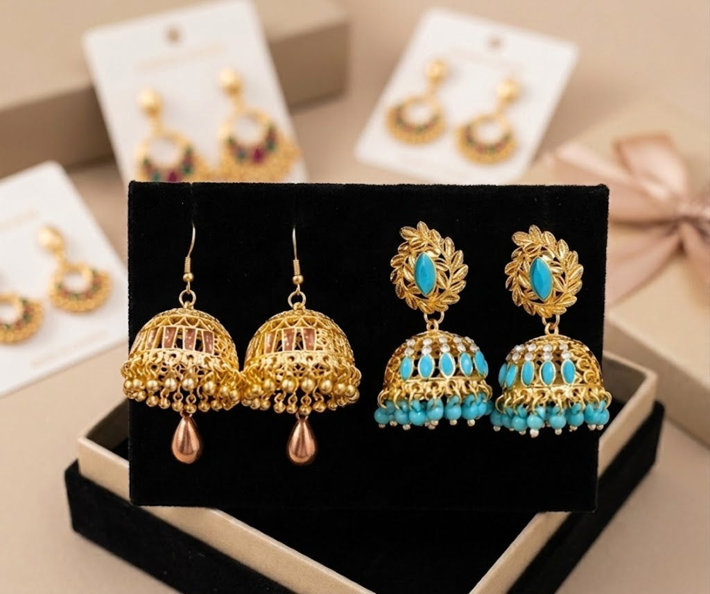 Gold-toned traditional Indian jhumka earrings with turquoise blue stones, displayed on a black velvet jewelry box with additional pairs on white cards in the background.