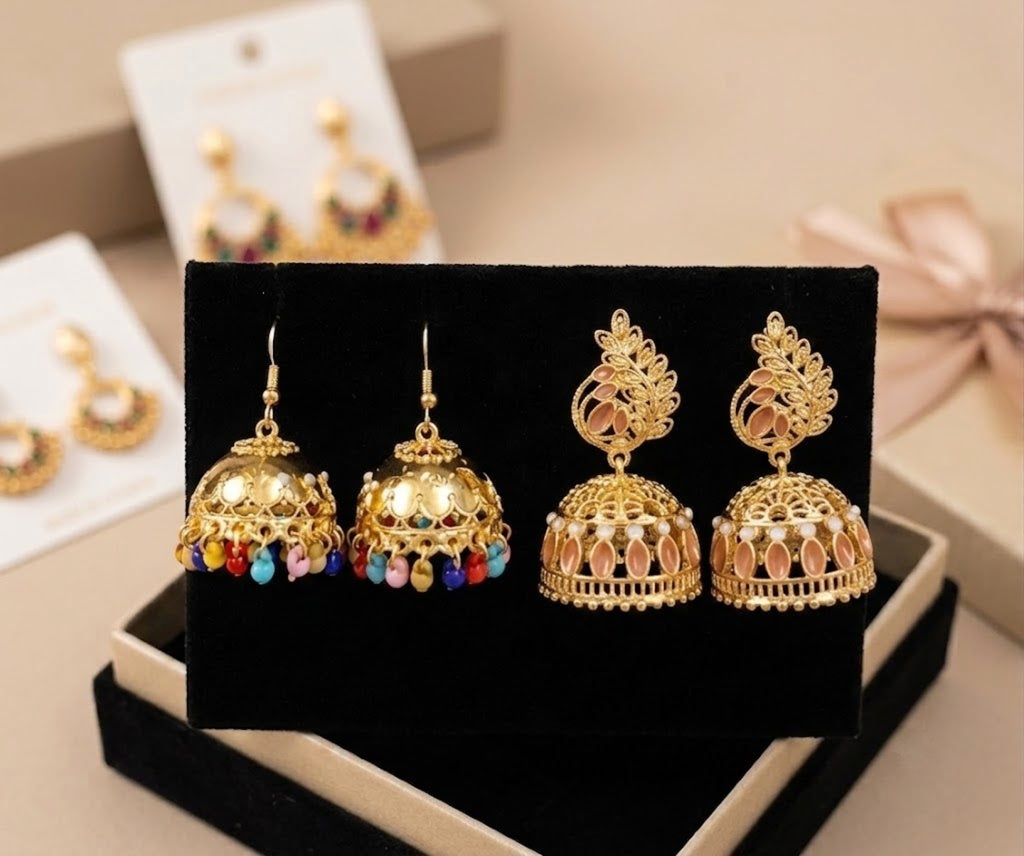 Gold-toned traditional jhumka earrings displayed on a black velvet jewelry box, with additional pairs on white cards in the background.